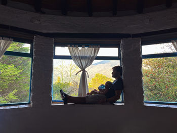 Rear view of woman sitting on window