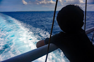 Rear view of boy leaning on boat railing in sea