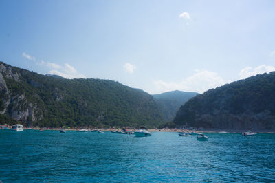 Boats on mediterranean sea by mountains against sky at cala goloritze