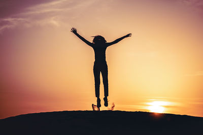 Silhouette man with arms outstretched standing against sky during sunset