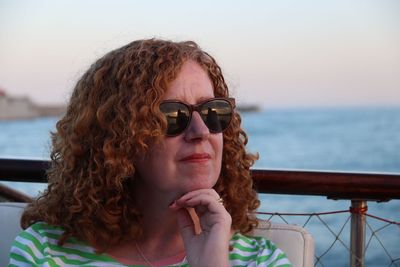 Thoughtful woman wearing sunglasses against sea during sunset