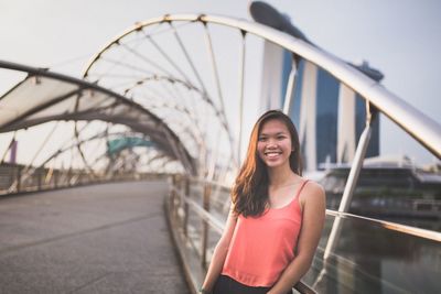 Portrait of young woman smiling on bridge in city