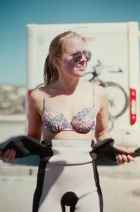 Young woman wearing sunglasses and bikini top against sky