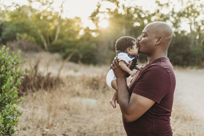 Close up of sweet father kissing newborn girl in backlit field