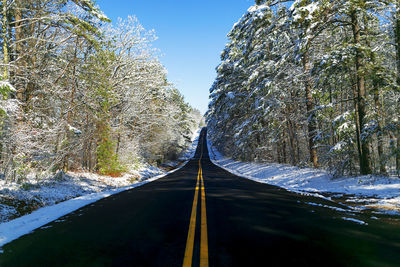 Road amidst trees and snow against sky