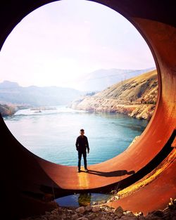 Portrait of man standing on large circle pipe with river in background at dam
