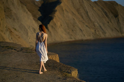 Rear view of woman standing on rock by sea