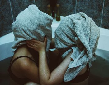 Lesbian couple embracing with towels on face in bathtub