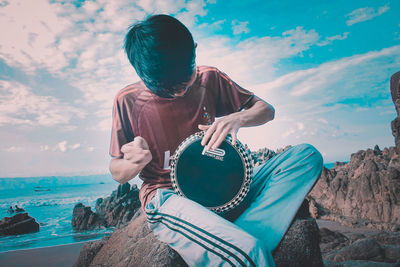 Woman sitting on rock by sea against sky