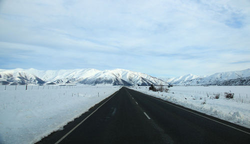 Road leading towards snowcapped mountains against sky