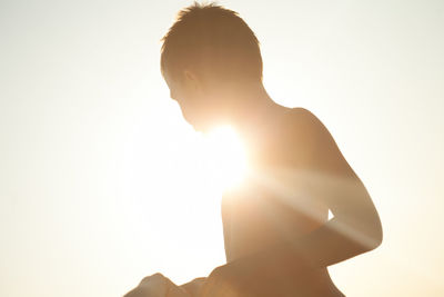 Silhouette shirtless boy against bright sky