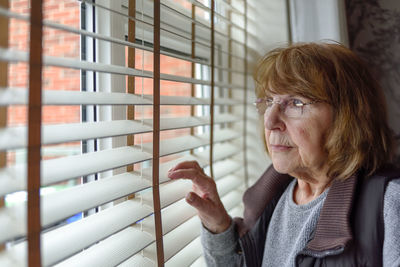 Close-up of woman looking through window at home