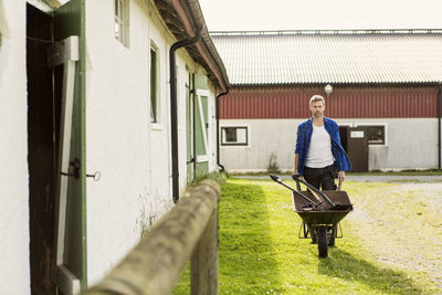 Man pushing wheelbarrow while walking by barn at farm