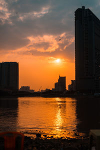 Buildings by river against sky during sunset