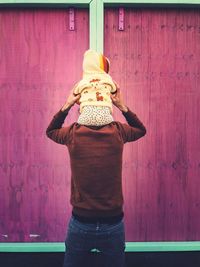 Rear view of father carrying daughter on shoulders against wall