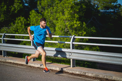 Young man jogging on by railing against sky