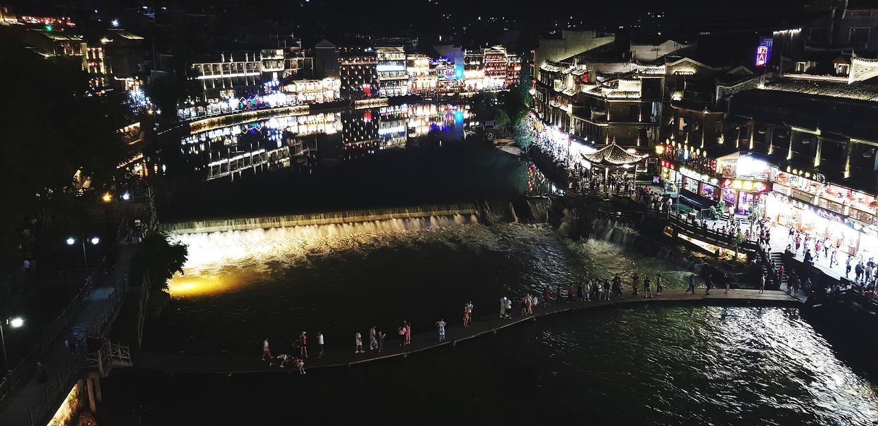 HIGH ANGLE VIEW OF ILLUMINATED BUILDINGS BY RIVER