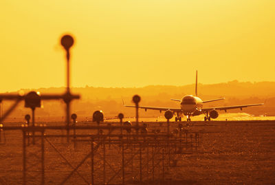 Silhouette airplane on airport runway against clear sky during sunset