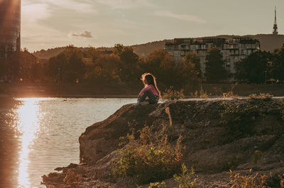 Girl sitting on land against sky during sunset