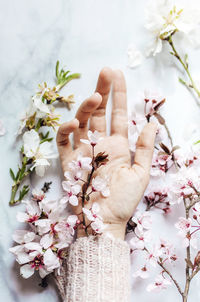 Female hand with pink almond flowers coming out of the sleeve on marble background. spring concept