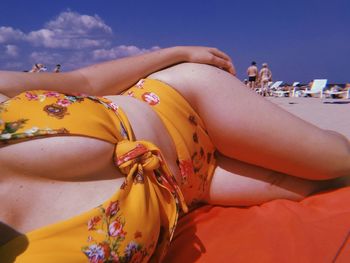 Midsection of seductive woman relaxing at beach against sky