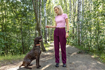 Portrait of a young blonde woman training a hunting dog of the kurz-haar breed in the park. 