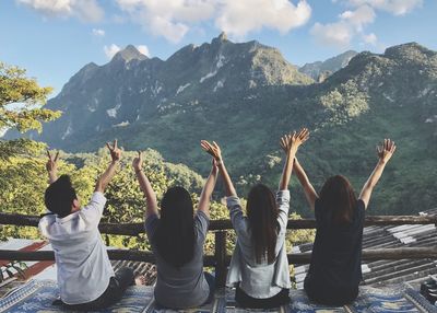 Rear view of friends sitting on mountain against sky