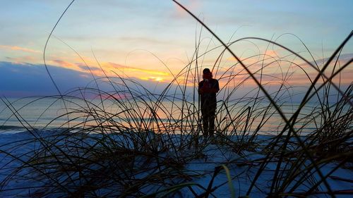 Silhouette man standing by sea against sky during sunset