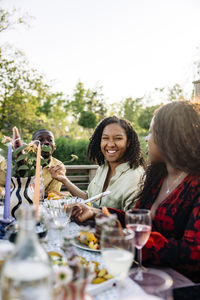 Smiling woman having food with friends sitting at dining table during party in back yard