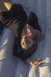 A young woman lies upside down and holds hand near his face on a white sheet 