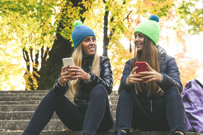 Two girls sitting in the park using smartphone. teen using mobile phone. sisters chat with friends.