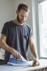 Young man ironing in house