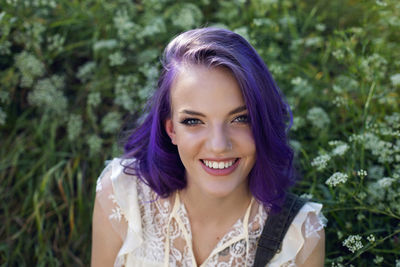 Portrait of a cheerful young woman with purple hair in summer on a green field