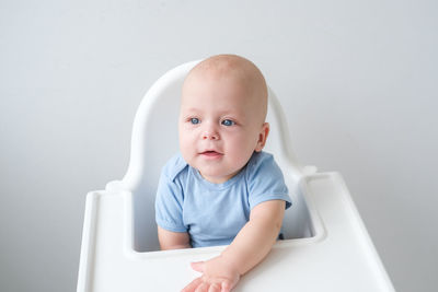 Portrait of cute baby boy sitting on table against wall
