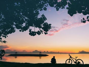 Silhouette bicycle by lake against sky during sunset