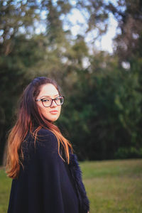 Portrait of young woman in warm clothing standing on grassy field at park