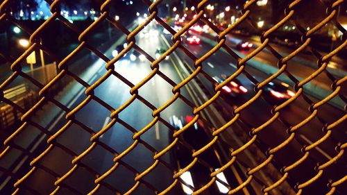 High angle view of street seen through chainlink fence at night