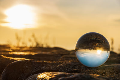 Close-up of crystal ball on shore against sunset