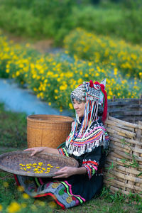 Midsection of woman sitting on yellow flower in field