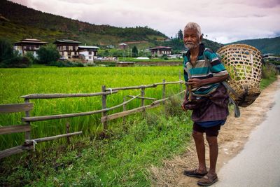 Full length of senior farmer with basket standing by agricultural field