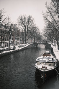 Boat moored in canal by city against sky