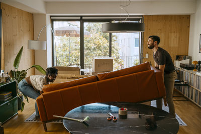 Multiracial couple helping each other while lifting sofa in living room at new home