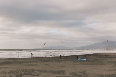 People at beach against cloudy sky