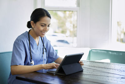 Smiling female doctor using tablet computer at table in hospital