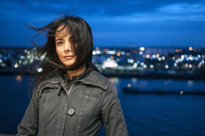Portrait of woman standing against cityscape at night