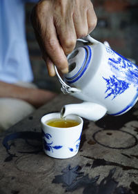 Close up photo of a man pouring tea from a ceramic teapot to matching cup