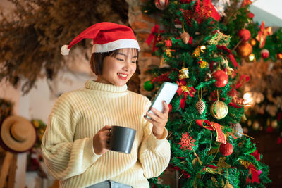 Smiling woman holding coffee cup standing against christmas tree