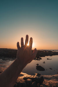 Person hand at beach against sky during sunset