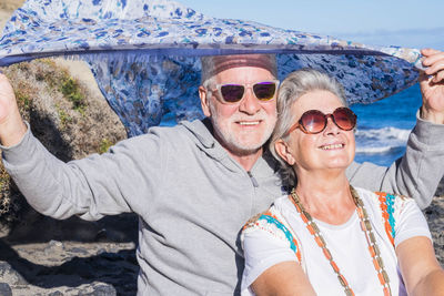 Happy senior couple with scarf sitting at beach