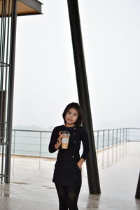 Portrait of young woman holding coffee while standing on building terrace